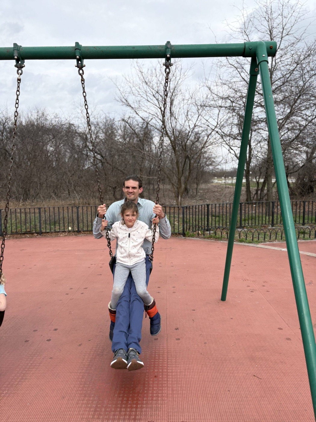 Sam pushing his daughter on a swing at the playground